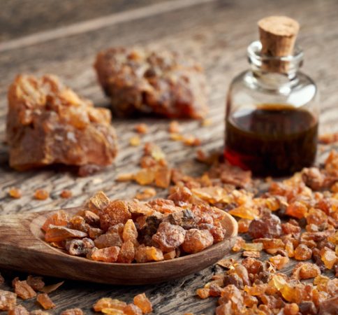 Myrrh resin on a spoon, with myrrh essential oil in the background